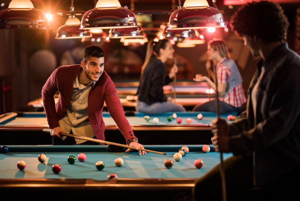 Happy man talking to his friend while playing snooker in a bar.