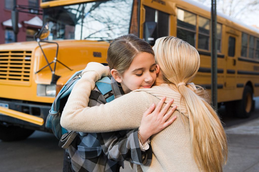Girl and mother hugging by school bus