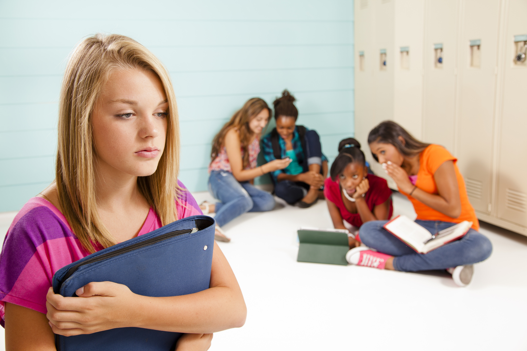 Teenage girls cyber-bully classmate. Gossip, talking. School hall. Lockers.