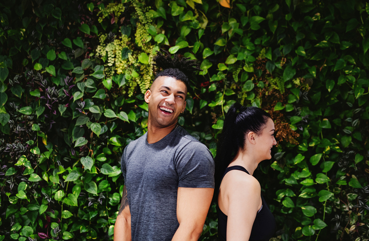 Side view of young couple standing back to back outdoors against green background.