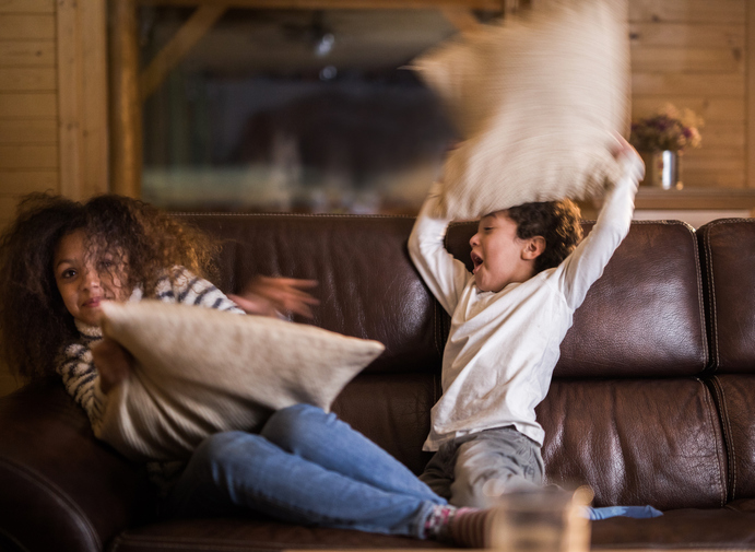Playful African American girl and boy having a pillow fight at home.