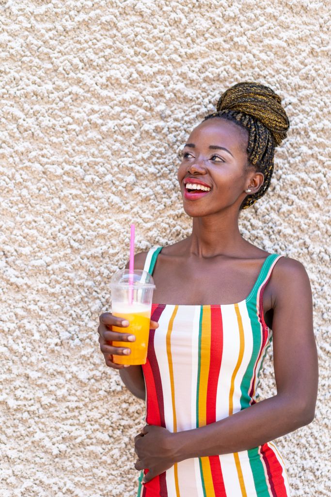 African woman leaning back on a wall and drinking fruit juice