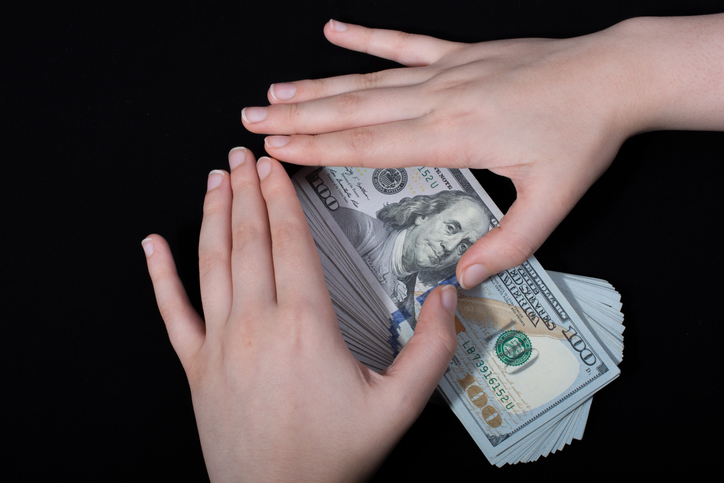 Cropped Hands Of Woman Making Heart Shape On American One Hundred Dollar Bills Over Black Background