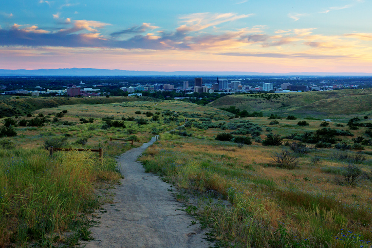 Foothills hiking trail leads downhill toward Boise skyline at sunset, summer evening in Idaho