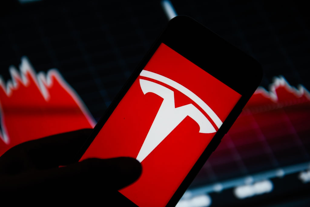 In this photo illustration a Tesla logo seen displayed on a...