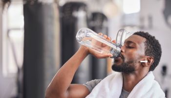 Water bottle, tired black man in gym and resting after fitness workout, healthy sports exercise and muscle growth training. Rest, motivation and thirsty athlete drinking water for hydration wellness