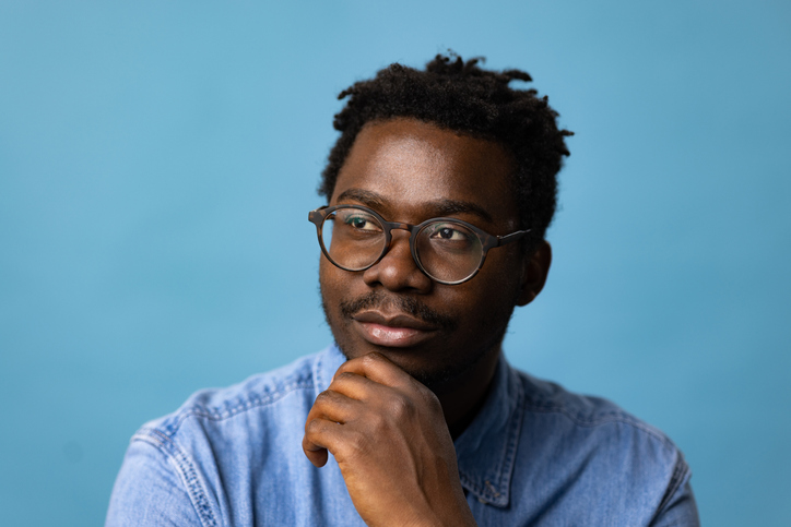 Young black man day dreaming against blue background.