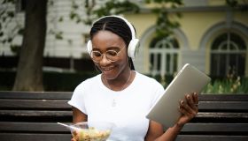 Portrait of a young African woman eating, using tablet and enjoying music outdoors