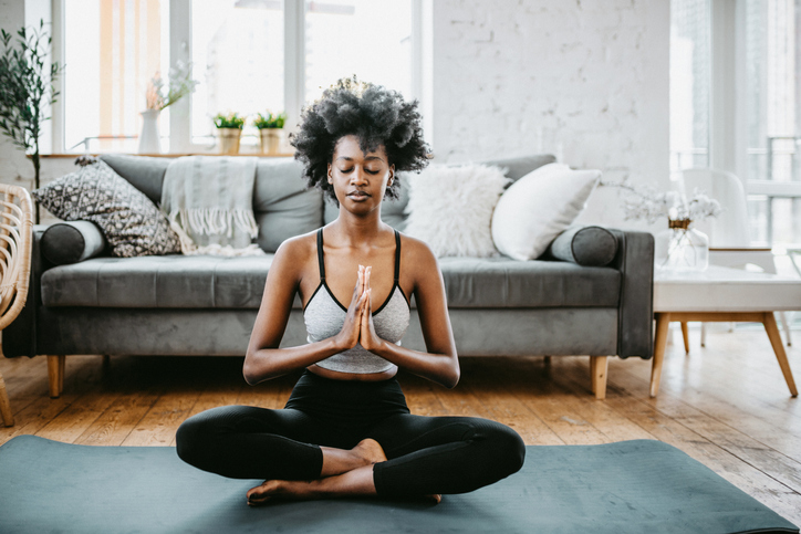 Doing yoga at home. Young black woman doing yoga relaxing exercises in living room. Lotus position