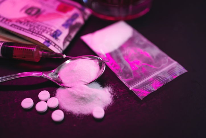 Neon-lit scene with white pills, syringe, powder and money banknotes on dark background, concept of drug addiction, substance abuse and nightlife risks