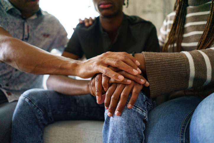 Close-up of mom and dad placing their hand over their son’s hand on his knee.