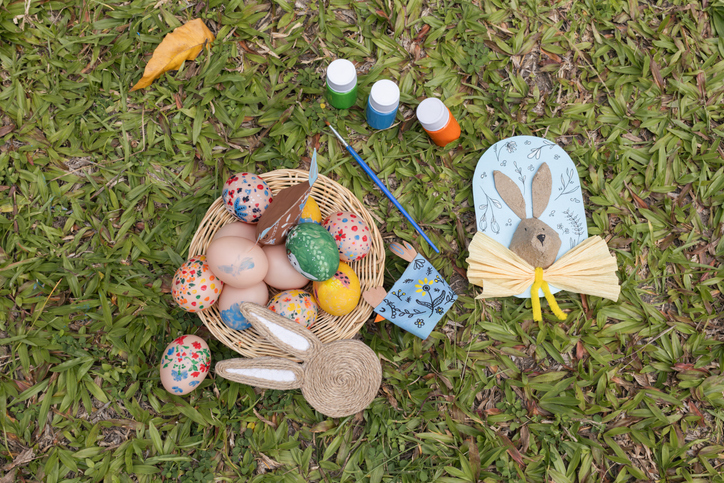 Top View of Painted Easter Eggs, Paints and Handmade Bunny and Chick Decorations on Grass