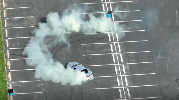A car emitting smoke and steam on a racetrack, with visible lines and markings on the surface.