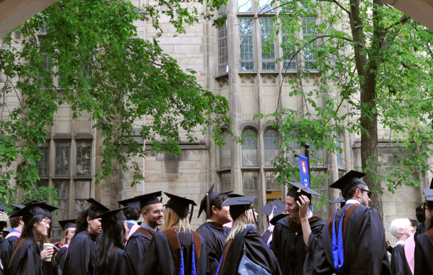 A group of graduates in academic regalia standing in front of a building with ivy-covered walls.