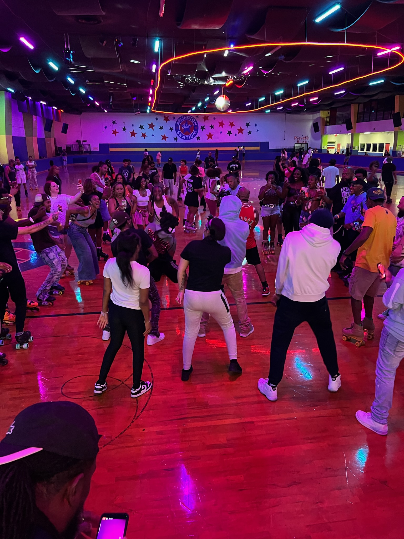 A crowded dance floor with people dancing and socializing in a brightly lit, neon-colored venue with the "Club Rewind" logo visible.