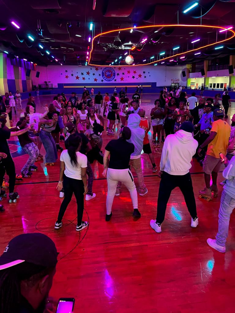 A crowded dance floor with people dancing and socializing in a brightly lit, neon-colored venue with the "Club Rewind" logo visible.