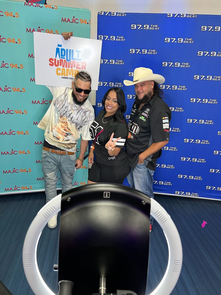 Three people posing in front of a "MAJIC 94.5" backdrop, with a radio station logo and frequency visible.