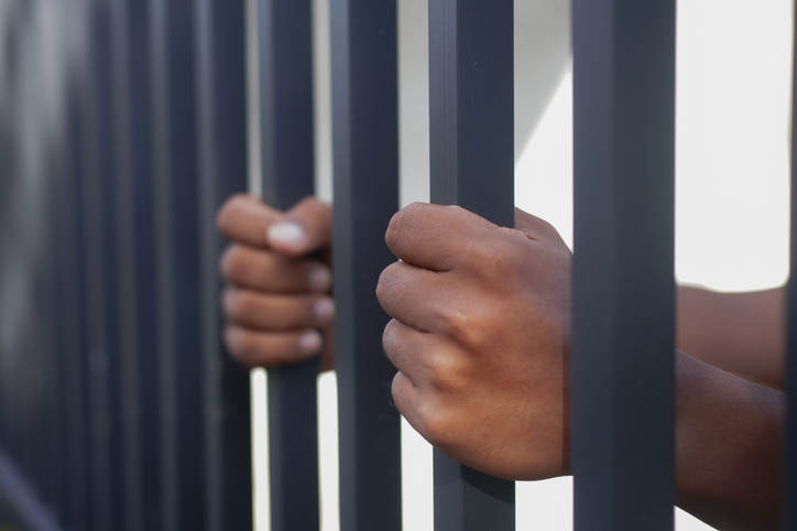 Close-up of hands gripping metal prison bars, symbolizing imprisonment, justice, crime, human rights, freedom restriction, and social issues. Concept of detention, punishment, and captivity.