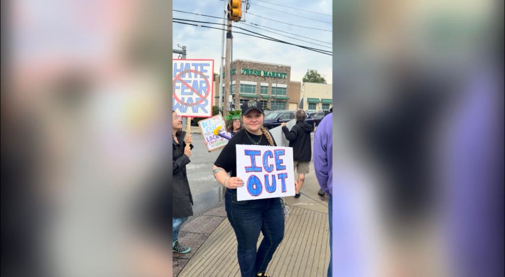 A person holding a sign that says "ICE OUT" while participating in a protest or demonstration.