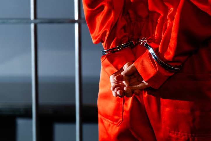 Prisoner in jumpsuit with handcuffed hands behind back in prison