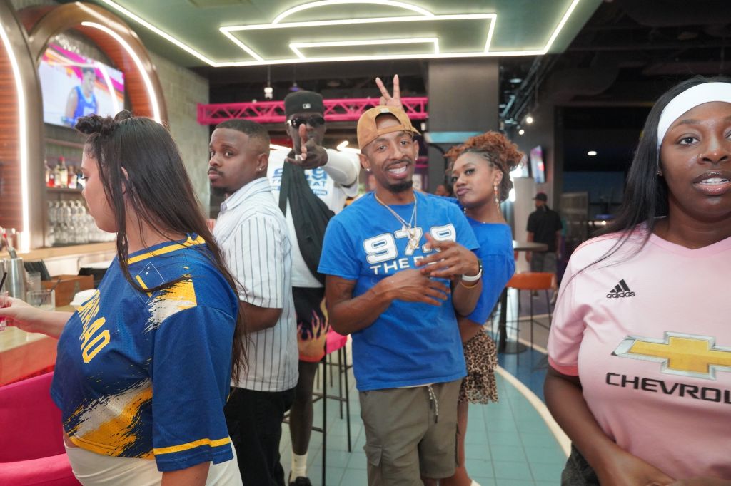 A group of people, some wearing sports jerseys, posing and making gestures in an indoor setting with neon lighting and decor.