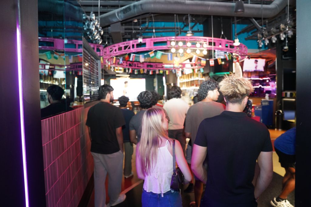 Crowded indoor venue with colorful lighting, decorations, and people socializing.
