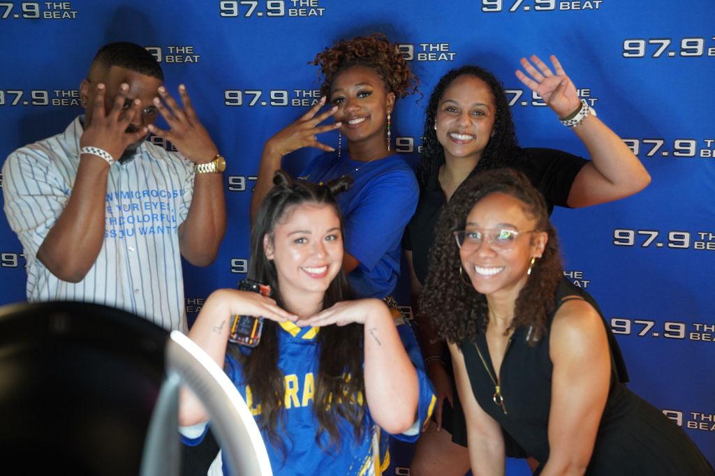 A group of four smiling people posing in front of a backdrop with the text "97.9 THE BEAT".