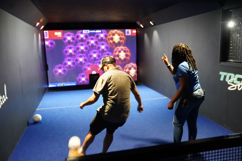 Two people playing a video game with colorful, abstract visuals displayed on a large screen.