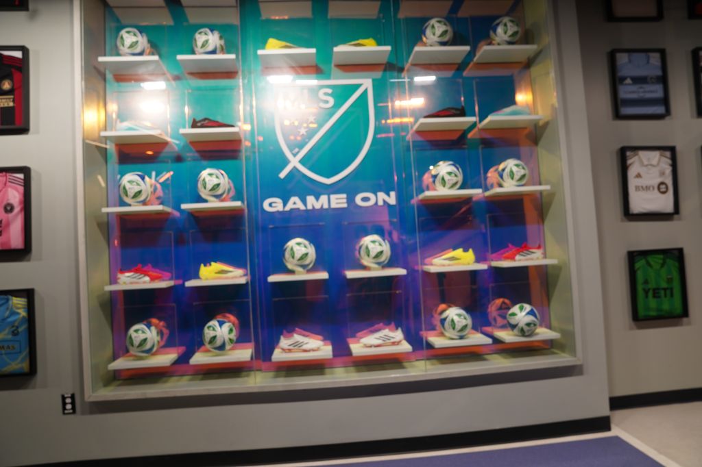 Shelves displaying various sports equipment and apparel, including soccer balls and shoes, with a "Game On" sign in the center.