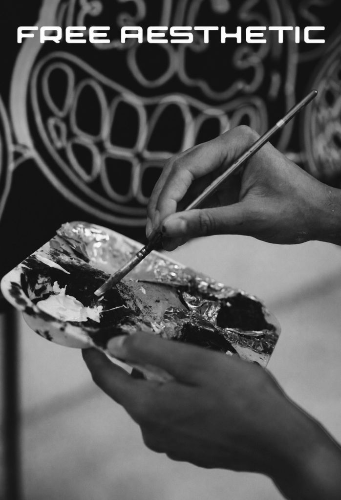 A hand holding a paintbrush, painting on a textured surface. The text "FREE AESTHETIC" is visible in the background.
