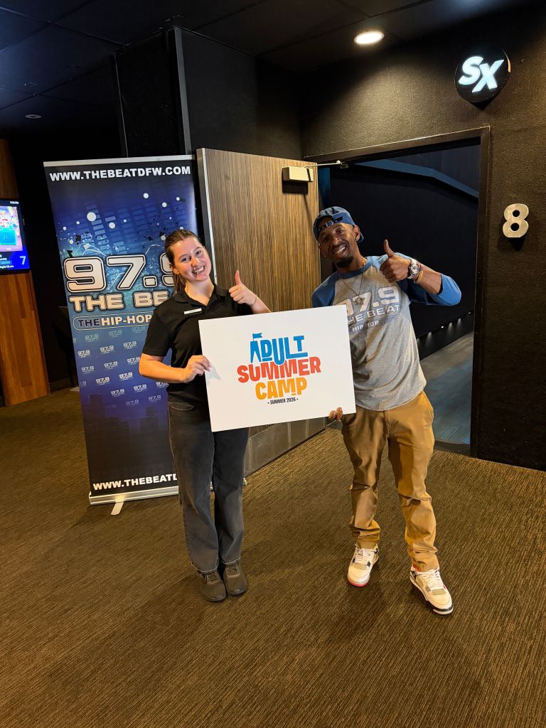 Two people holding a sign for "Adult Summer Camp" in a radio station studio with "97.9 The Beat" branding visible.