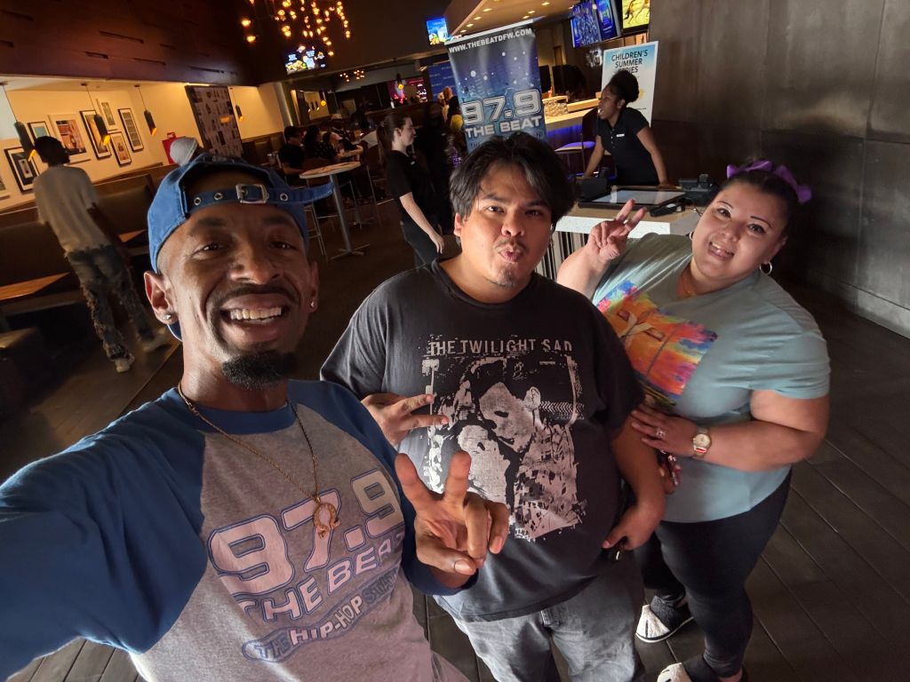 Three people smiling and posing for a photo in a crowded bar or restaurant, with "97.9 The Beat" signage visible in the background.